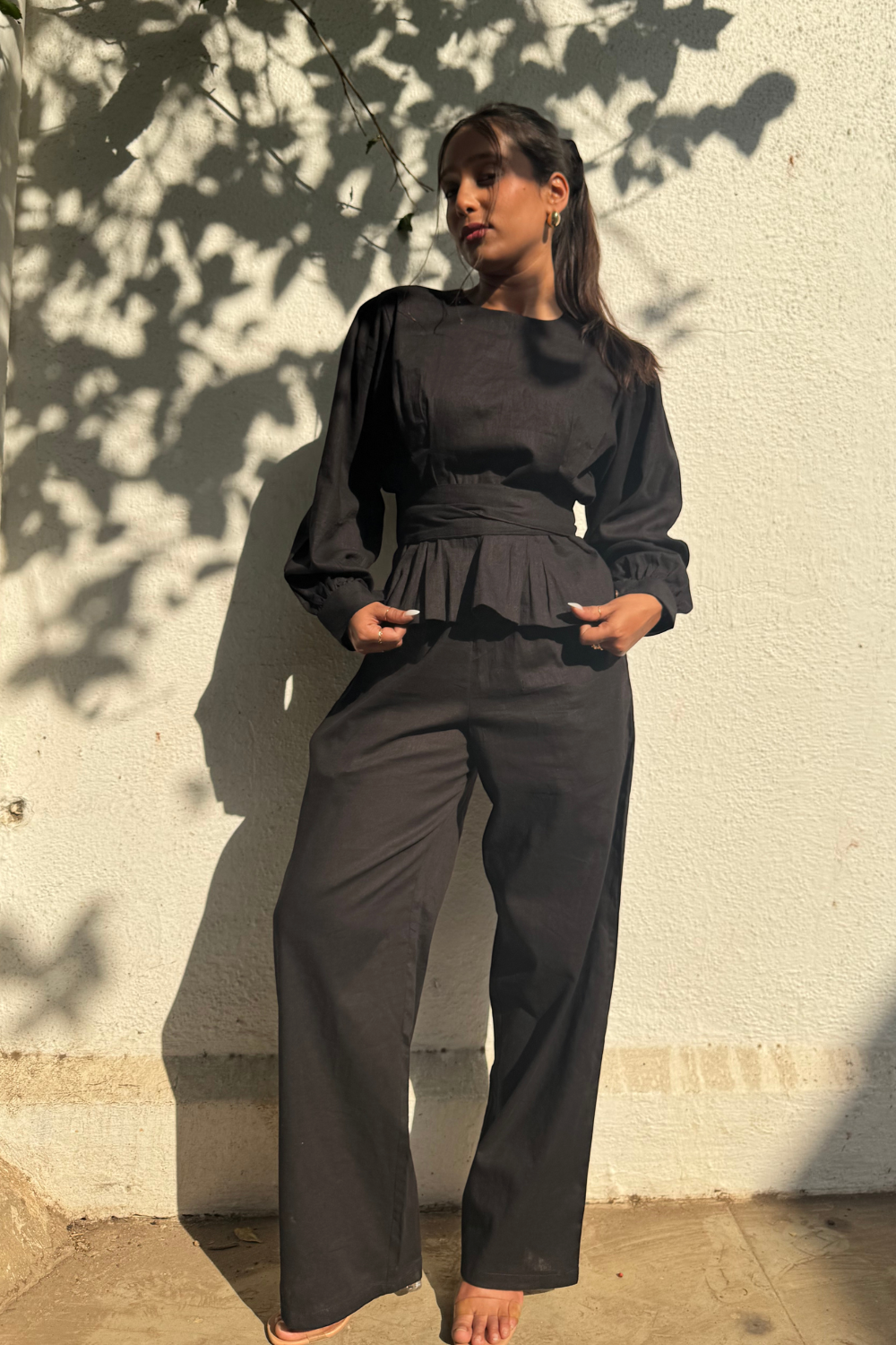 A woman wearing a black co-ord set with tie-around detail, consisting of a top with puffed sleeves and wide-leg pants.