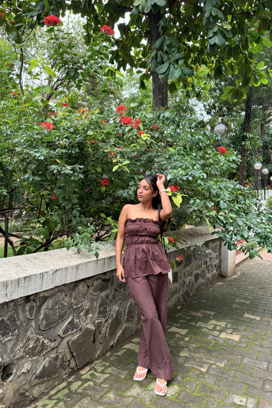 Woman in a BROWN outfit standing in a garden with greenery and flowers.